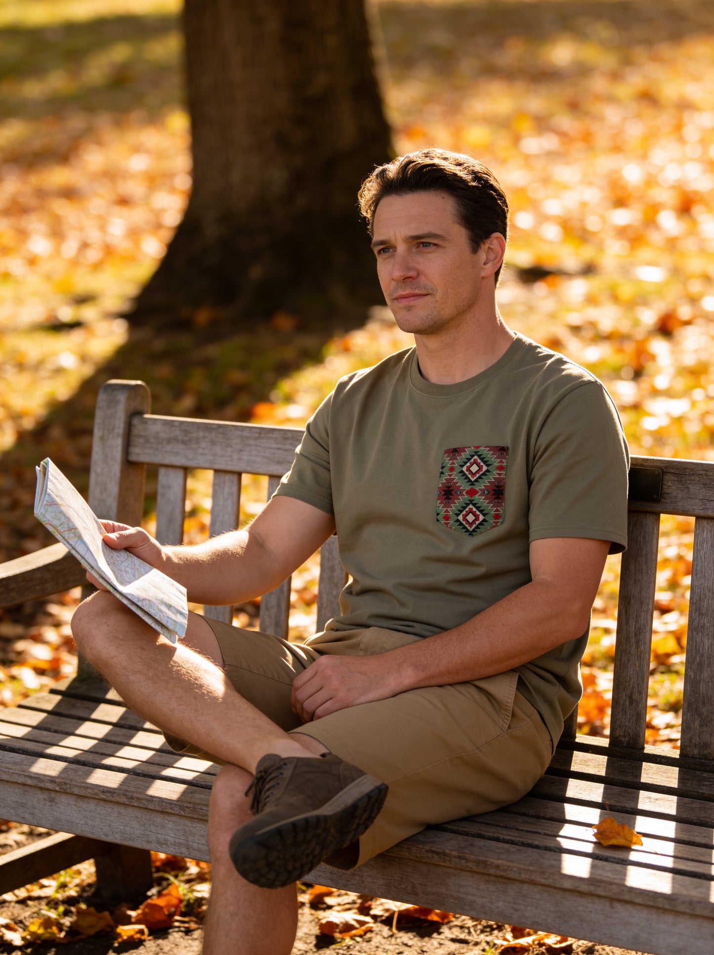 Man sitting on a bench in an autumn park reading a book.