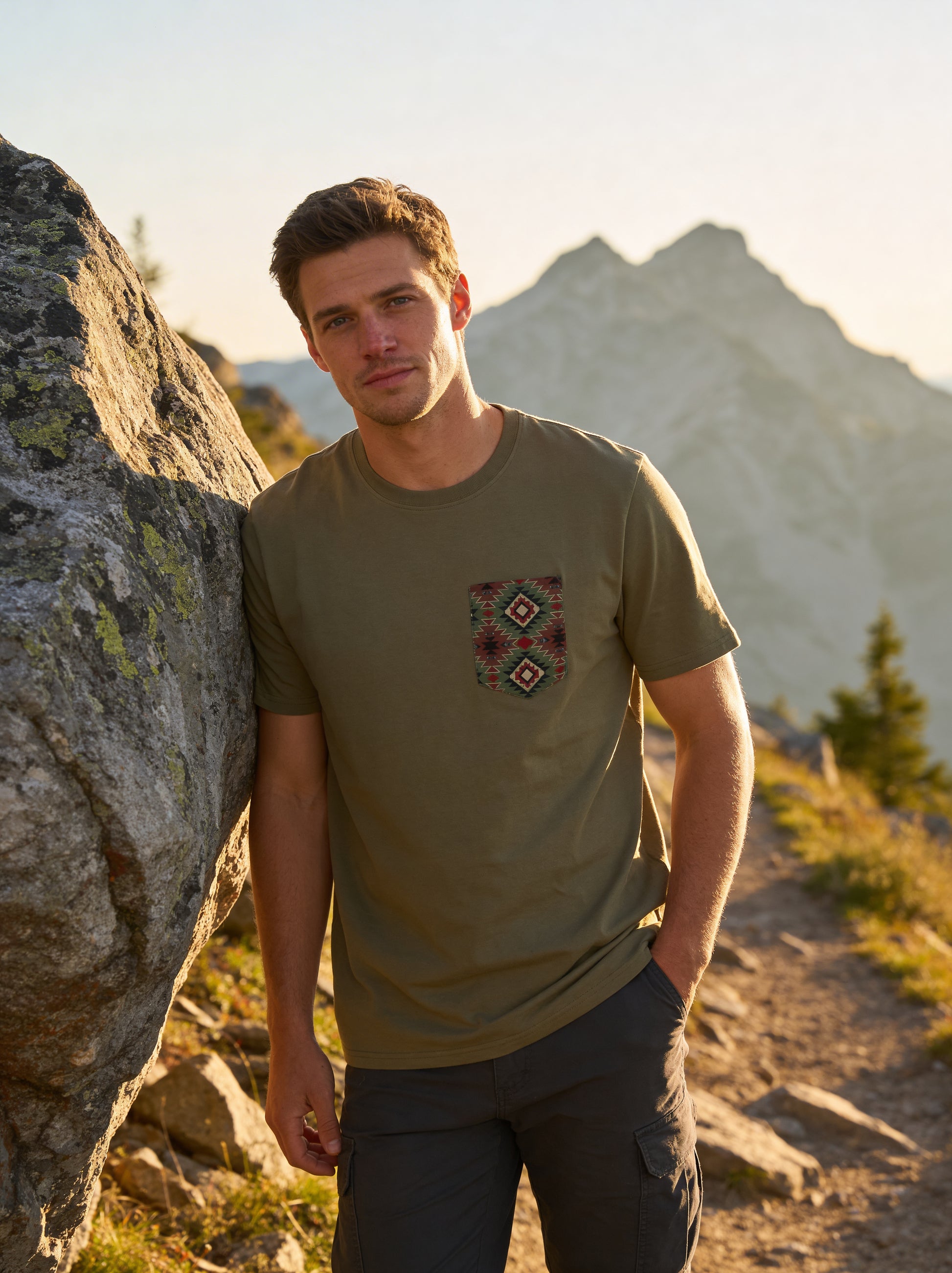 Man standing outdoors with mountains in the background wearing a green t-shirt with a pocket design.