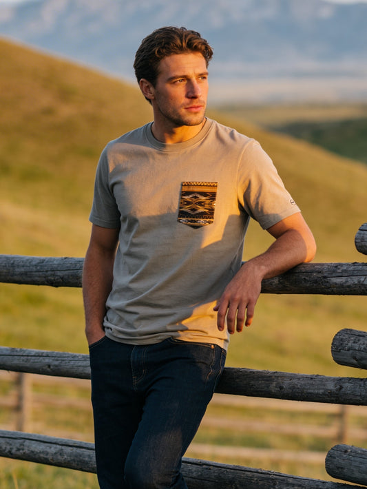 Man leaning against a wooden fence in a scenic landscape with rolling hills.