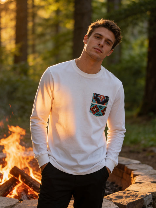 Person wearing a white sweatshirt with a colorful patch in front of a campfire in a forest.